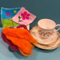 Needle felting yarn, sponge and needle next to a vintage tea cup and saucer