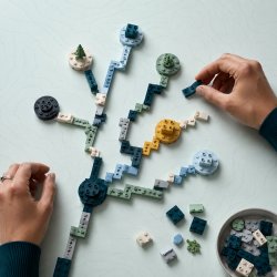 Hands arranging teal, green, blue, and gold building bricks into a branching career map with several possible paths.