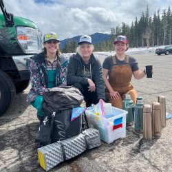 3 guides and volunteers pose together in a mountain parking lot while serving hot cocoa on a winter trip