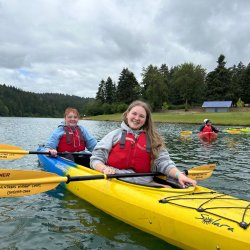 2 people paddle a tandem kayak on Hagg Lake while wearing P-F-Ds (lifejackets)