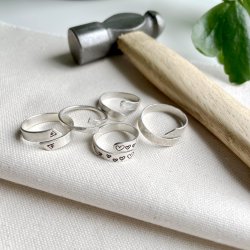 A group of five silver wrap rings, two with stamped designs next to a jewellers hammer