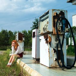 Woman sitting next to derelict petrol pumps