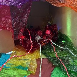 Lights nestled in coloured plastic contained in a cardboard box on it's side. Coloured plastic and laces trailing out of the box.