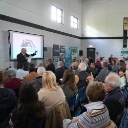 Attendees at the landlord forum sat in rows, watching a presentation from one of the speakers who is stood at the front, holding a microphone