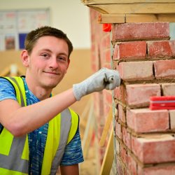 A male student is smiling in a brickwork workshop.
