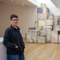 The artist Eva Rothschild stands beside her work Amphi that are colourful large blocks piles high by the back wall.