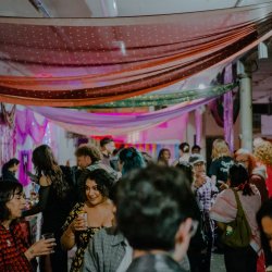 a long room with draped sarees criss crossing the ceiling is shown with people mingling with drinks and chatting