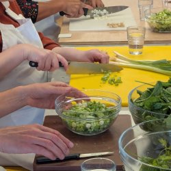 A group of people prepare a shared meal together at a long rectangular table while engaging in conversation.