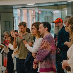 A group of people chatting and looking onto an exhibition that is not visible in the image. Someone is taking a photo on the their phone.