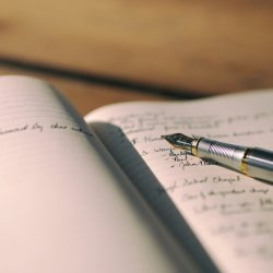 A handwritten note pad with a fountain pen sat on top