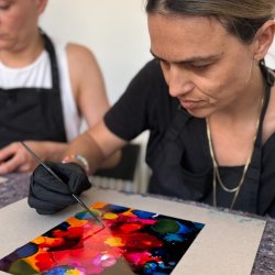 Two participants creating colorful alcohol ink artworks in a bright artist studio.