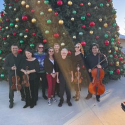 Musicians standing in front of a Christmas tree.