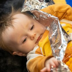 A young baby laying on a textured black mat playing with a long piece of foil.