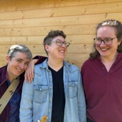 Patti Powell, Erinn Doncaster, and Ali Romanow standing in front of a wood wall, laughing