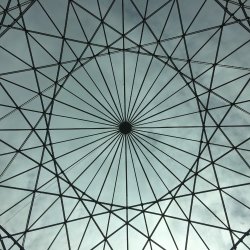 Glass roof intricately supported by tie-bars, creating a self-supporting structure. The photo is taken from underneath dead-centre to reveal the circular symmetry of the structure