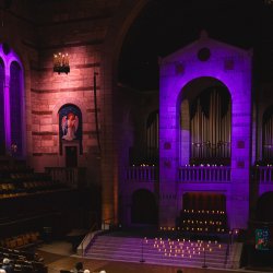 an image of the Fountain Street Church sanctuary, with the central arch lit in purple and an angel on the left lit in amber.