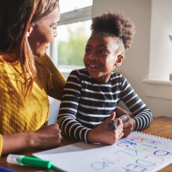 Mum and daughter smile at each other while working on spelling homework