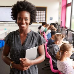 A teacher smiling while primary school age children work on computers behind her