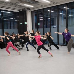 Image features NYB All In! participants dancing Ballet in a light studios with floor length windows.