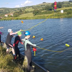 Young lifesavers wearing wetsuits use throw bags next to the river