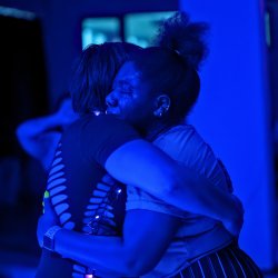 Black woman with eyes closed and tears being held by another woman.