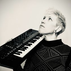 Person holding a small keyboard synthesizer on their shoulder, looking upward.