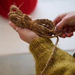 Close up photograph of hands delicately holding a ball of hop yarn. Person is wearing a mustard coloured mohair jumper.