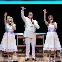 3 singers on stage in white outfits
