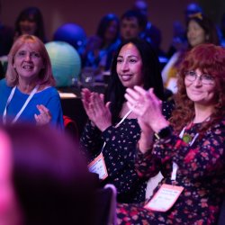 A group of people smiling and clapping. Sat down at an Awards event.