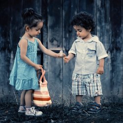 Two young children are playing. A girl holding a bag offers a boy a flower