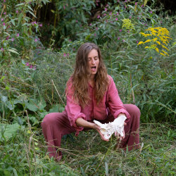 A woman in squat, holding pelvic bones in front of her and sounding with eyes closed.
