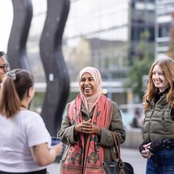 4 students smiling at each other standing next to wavy bacon statue on campus