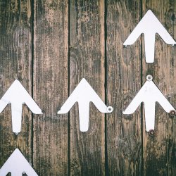 White arrows pointing upwards against a wooden background