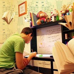 Teenage boy sitting writing at desk surrounded by notes