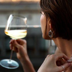 A crystal glass filled with red wine, set against a backdrop of a deep blue sky and lush green fields, capturing the essence of a perfect wine-tasting moment.