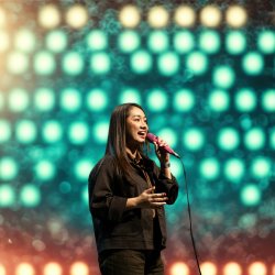 A smiling woman is singing into a microphone and gesturing