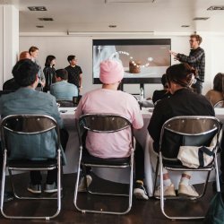 3 people sat on chairs looking at a man presenting.
