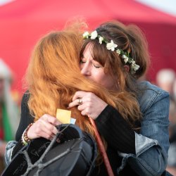 two women hugging in gratitude, one wearing a flower crown and holding a drum