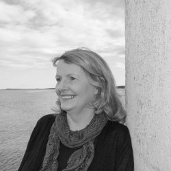 A black and white picture of a head and shoulder pic of Helen Forbes leaning against a wall overlooking a seaview