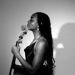 A side profile, black and white photo of Ayanna Witter-Johnson, holding her Cello against a plain backdrop