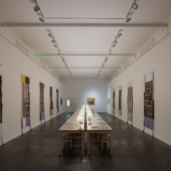 A long table fills a rectangular room. Small white are placed along the length of the table and fabric banners hang on the white walls.