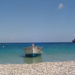 a fishing boat on the sea next to a pebble beach