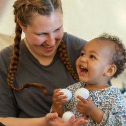 A young baby and their carer playing with white egg shakers
