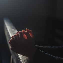 Hands held in a classic prayer pose, resting on what looks like a church pew