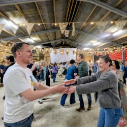 A couple smile at each as they begin to spin at the top of an Orcadian Strip the Willow last ceilidh dance. Bunting hangs from the barn roof. Dancers are smiling and laughing.