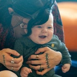 A young baby giggling sat in the arms of their carer