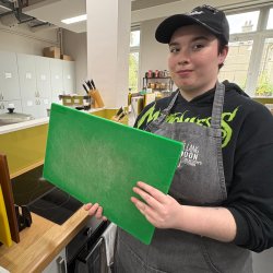 A woman's hand slicing yellow and red peppers on a green chopping board.