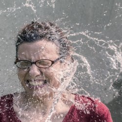 A woman has her face splashed with a large amount of water, she seems happy enough