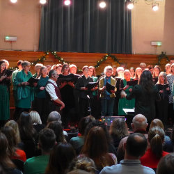 The image features the Cecil Sharp House Choir standing and singing in font of an audience