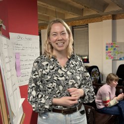 A white smiling woman stood in front of annotated flip chart paper